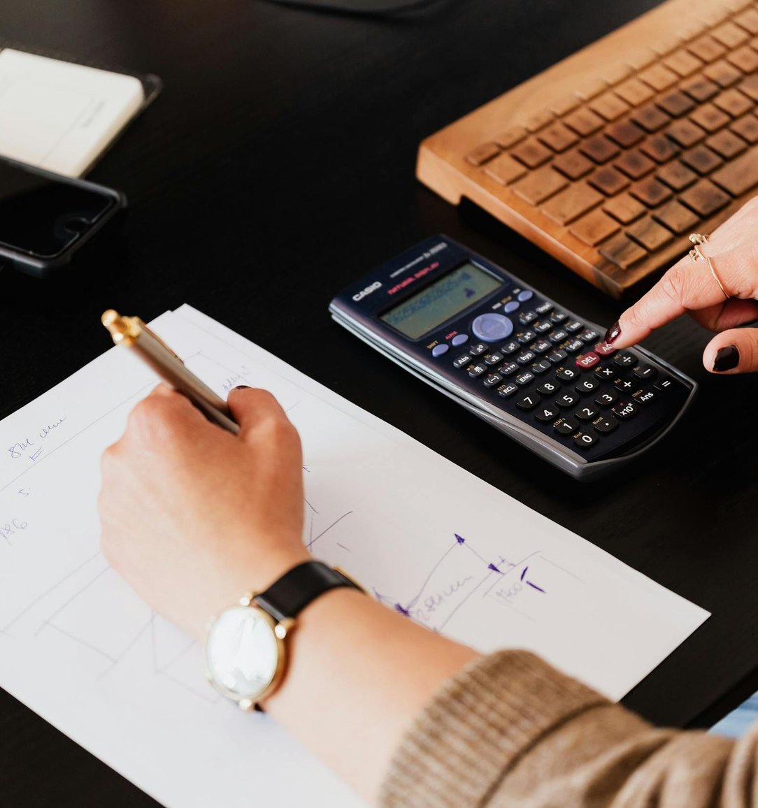 Bookkeeper writing notes on a financial worksheet beside a calculator